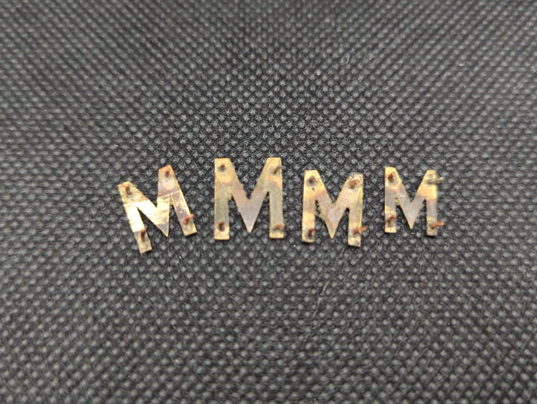 Four yellow metal letter 'M' appliques, gross weight 2.4 grams.